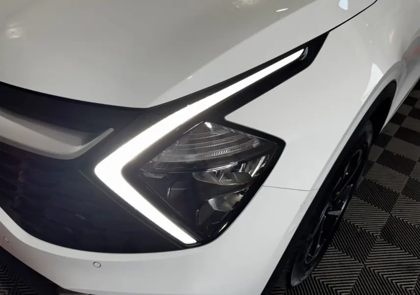 Gros plan sur le phare avant droit blanc du Kia Sportage 2024 avec signature lumineuse LED en forme de flèche.