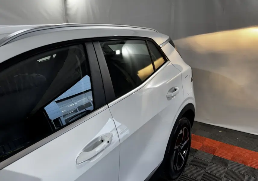 Vue côté droit arrière du Kia Sportage blanc 2024, avec poignées de porte et jante noire visible sur sol à motifs rouges et gris.