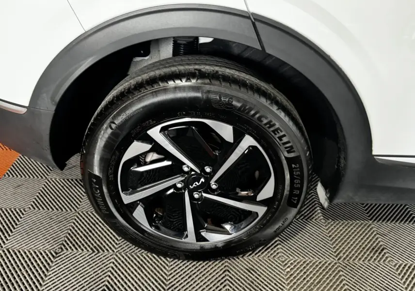 Gros plan sur la roue arrière droite d’un KIA Sportage blanc 2024 avec jante alliage noire et argentée.