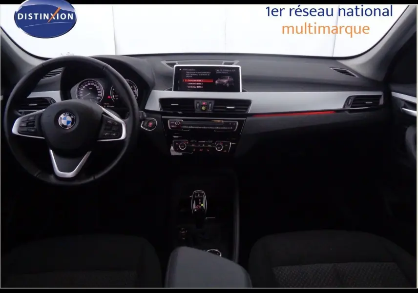 Intérieur avant d'une BMW X1 blanc Alpine, tableau de bord moderne avec écran central et volant multifonction noir.