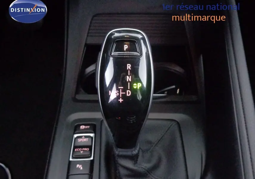 Le levier de vitesses automatique noir brillant de la BMW X1 blanc Alpine, vu en gros plan intérieur.