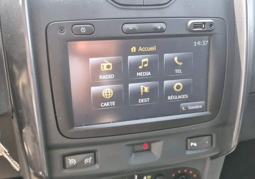 Vue rapprochée de l’écran tactile central du Dacia Duster 2015 gris foncé, affichant le menu principal avec options multimédia.