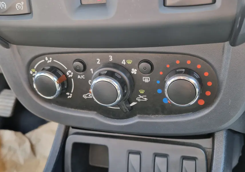 Gros plan sur les commandes de climatisation du Dacia Duster 2015, avec boutons ronds chromés et réglages manuels.