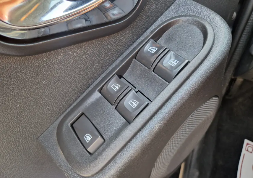 Gros plan sur les commandes de lève-vitres électriques côté conducteur du Dacia Duster gris foncé 2015.