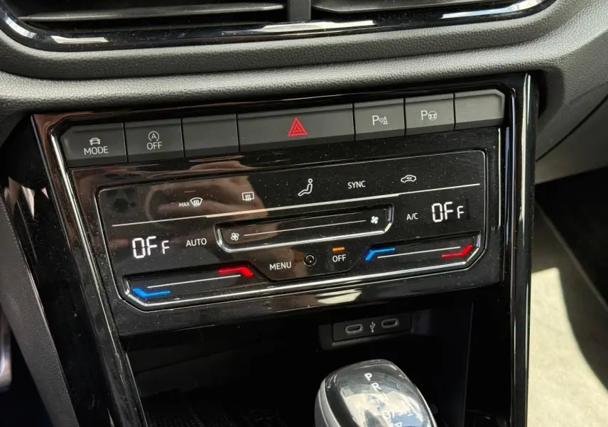 Vue rapprochée du tableau de bord noir brillant du Volkswagen T-Roc 2025, montrant la climatisation digitale et le levier de vitesse automatique.