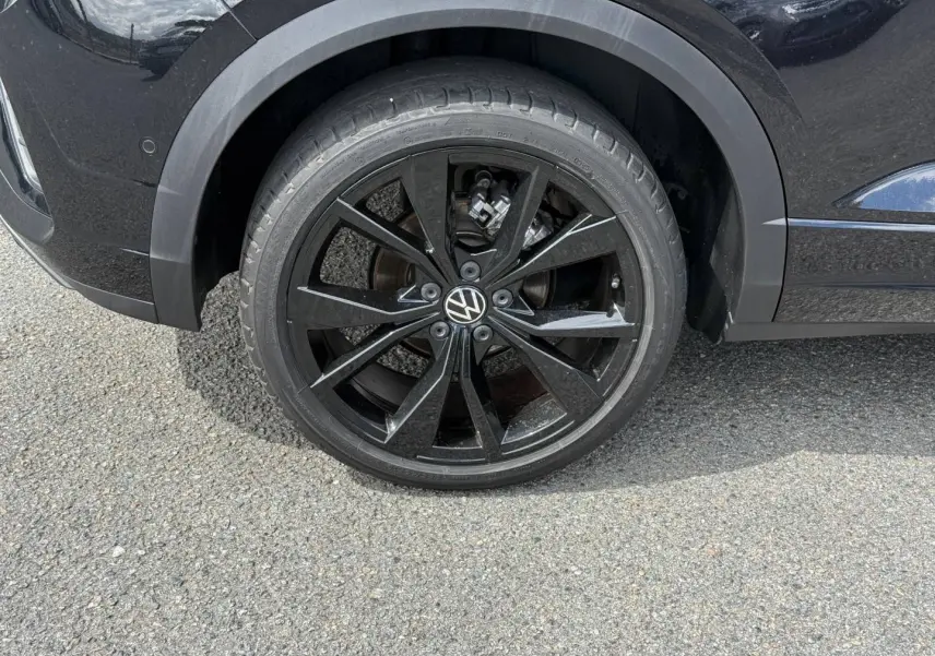 Gros plan sur la roue arrière droite noire brillante du Volkswagen T-Roc noir intense nacrée avec jante alu R-Line.
