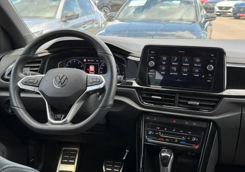 Vue intérieure du tableau de bord du Volkswagen T-Roc 2025, volant cuir multifonction et écran tactile central.