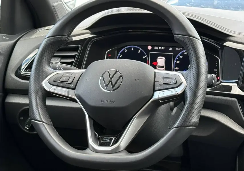 Vue rapprochée du volant cuir multifonction noir du Volkswagen T-Roc 2025 avec tableau de bord numérique en arrière-plan.