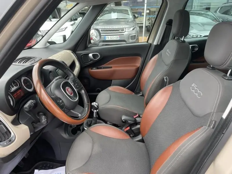 Intérieur avant droit de la Fiat 500L beige 2014 avec sièges gris et marron et volant bois noir.
