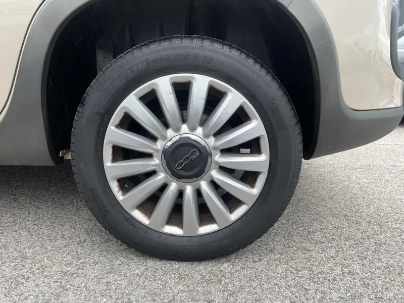 Gros plan sur la roue avant gauche beige d'une FIAT 500L 1.6 Multijet Tekking diesel de 2014 avec jante argentée.