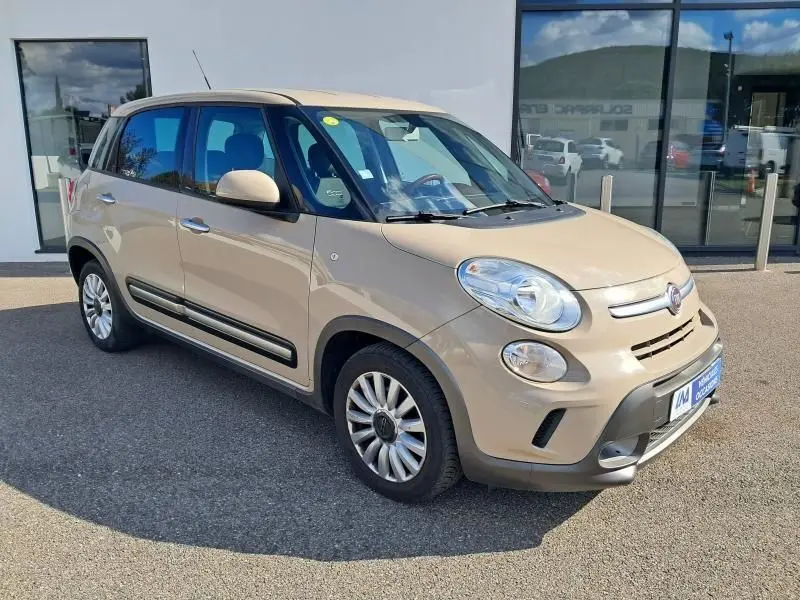 Fiat 500L beige vue 3/4 avant droit, montrant ses phares ronds et ses protections noires latérales.