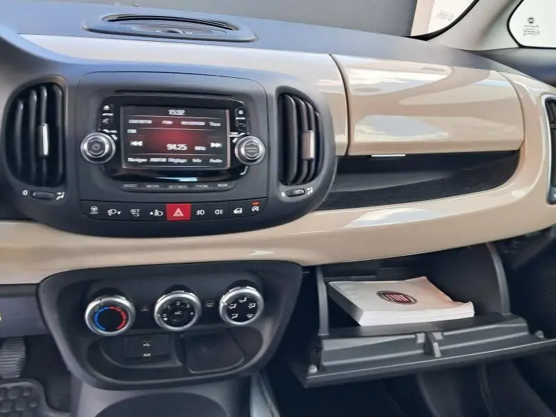 Tableau de bord beige de la Fiat 500L 2014, vue centrale avec écran radio et commandes de climatisation visibles.