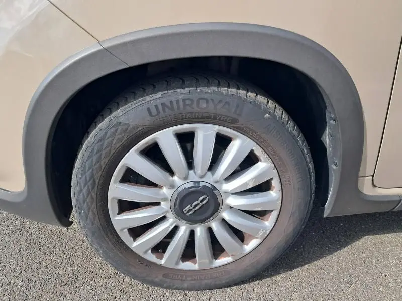 Gros plan sur la roue avant gauche beige d'une FIAT 500L 2014 avec jante multibranches et pneu Uniroyal.