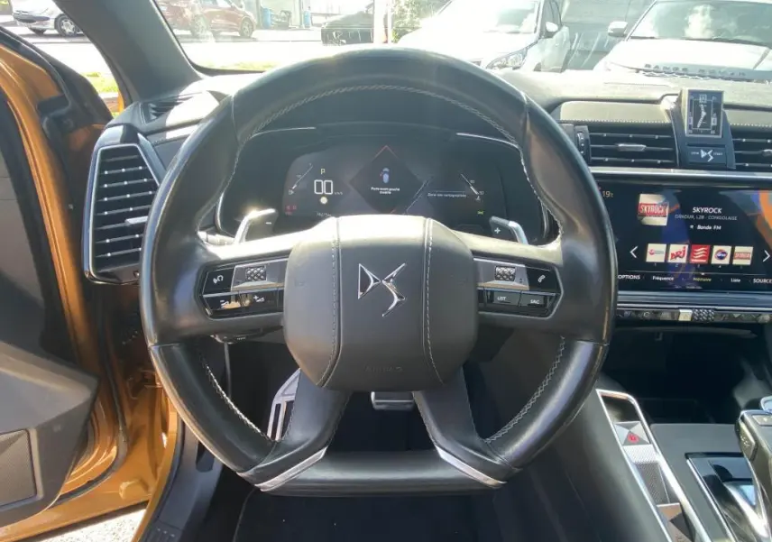 Vue centrée sur le volant cuir DS d'un DS7 Crossback jaune clair, avec tableau de bord numérique et écran tactile visible.