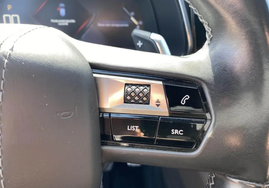 Gros plan sur les commandes gauche du volant noir du DS7 Crossback jaune clair, avec boutons LIST, SRC et téléphone.