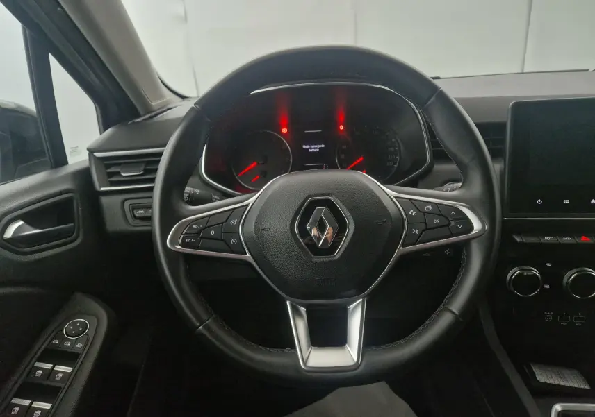 Vue centrée sur le volant du Renault Clio V gris platine, avec commandes intégrées et tableau de bord éclairé en rouge.