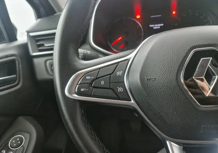 Gros plan sur le volant cuir noir de la Renault Clio V gris platine, avec commandes de régulateur de vitesse visibles.