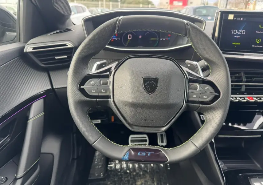 Vue intérieure centrée sur le volant GT noir avec surpiqûres vertes et tableau de bord numérique de la Peugeot 208 Hybrid 2025.