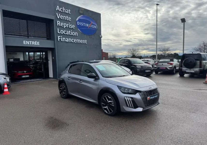 Peugeot 208 Hybrid gris vue 3/4 avant droit sur parking devant concession avec jantes alliage 17 pouces.