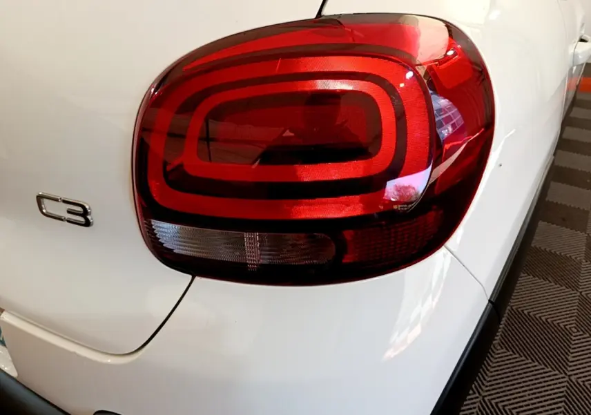 Gros plan sur le feu arrière droit rouge d'une Citroën C3 blanche, avec logo C3 visible sur la carrosserie.