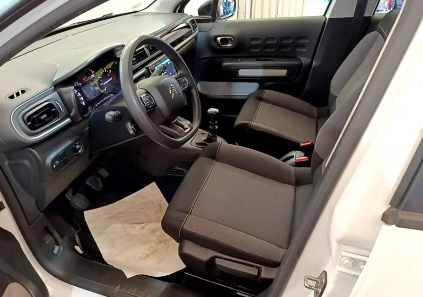 Intérieur avant droit d'une Citroën C3 blanche 2022, volant multifonctions, sièges tissu noirs et levier de vitesse manuel.
