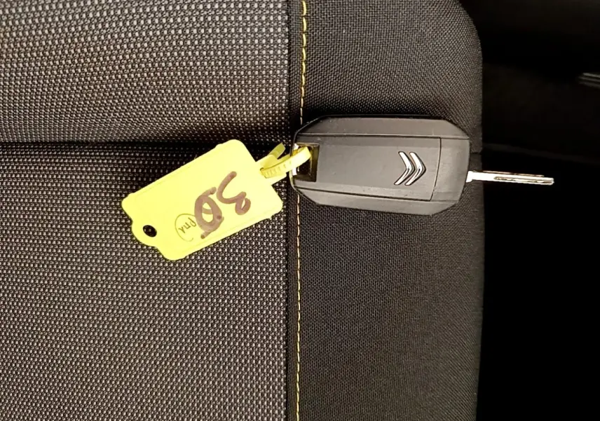 Clé de voiture Citroën posée sur un siège en tissu noir avec surpiqûres jaunes, étiquette jaune numérotée 30.