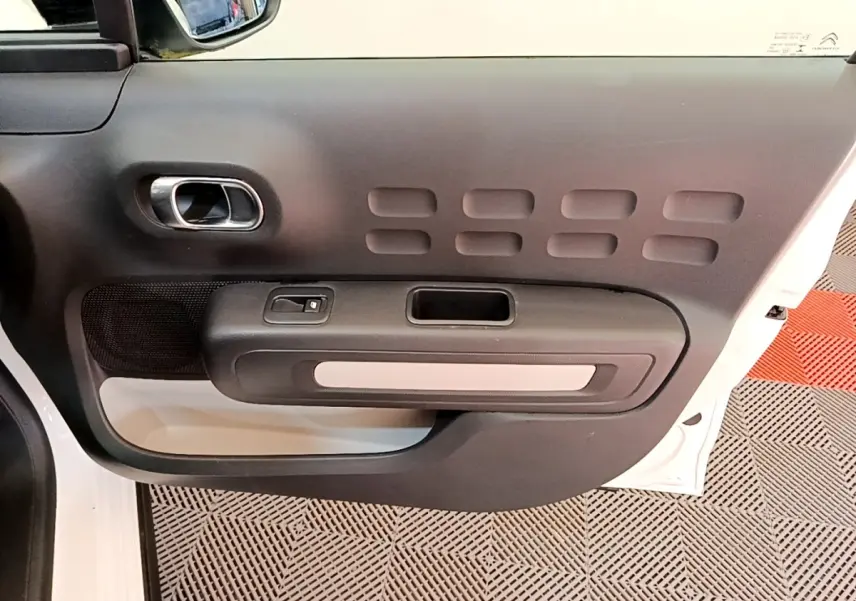 Vue rapprochée de la porte avant gauche blanche d’une Citroën C3 2022 avec poignée intérieure chromée et panneau noir texturé.