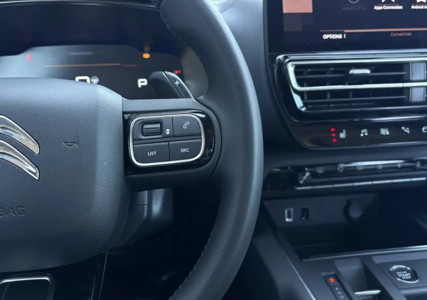 Gros plan sur le volant et la console centrale noire du Citroën C5 Aircross Hybrid 2025 avec commandes au volant et écran tactile.