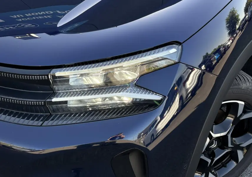 Gros plan sur le phare avant gauche et la jante diamantée noire du Citroën C5 Aircross Hybrid bleu Eclipse.