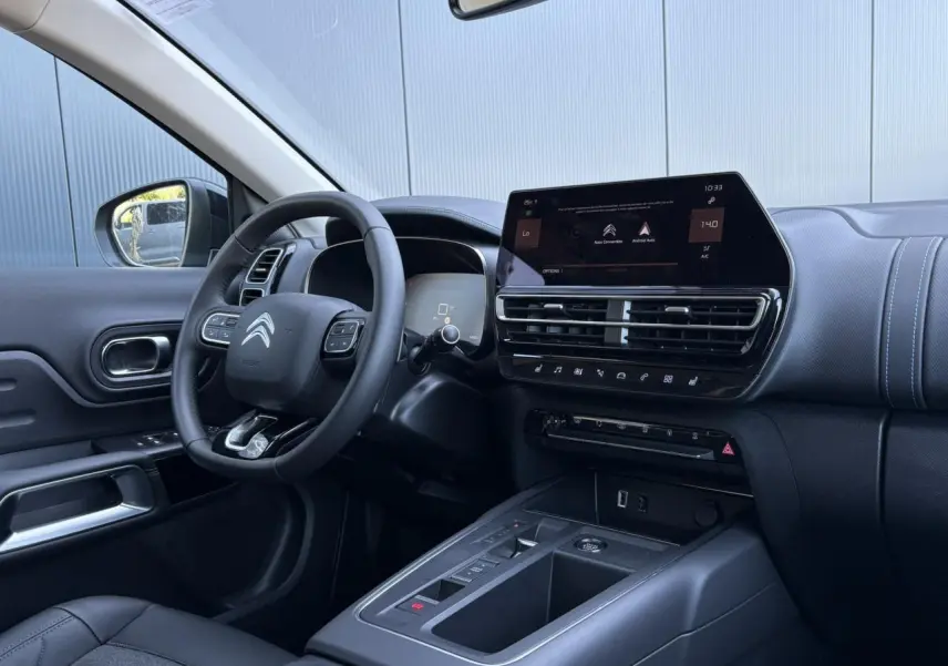 Vue intérieure côté conducteur du Citroën C5 Aircross Hybrid 2025, tableau de bord noir avec écran tactile et volant cuir.