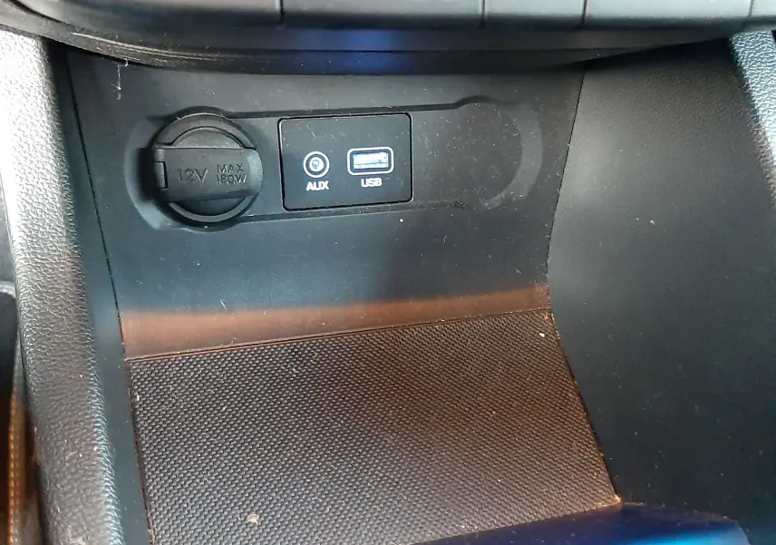 Détail de la console centrale noire de la Hyundai i20 2016 montrant prise 12V, entrée AUX et port USB.