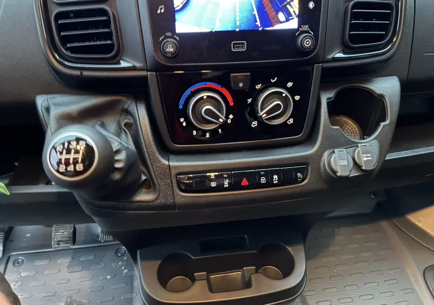 Vue rapprochée du tableau de bord noir du Fiat Ducato Fourgon 2025, avec levier de vitesse manuel et commandes climatisation.
