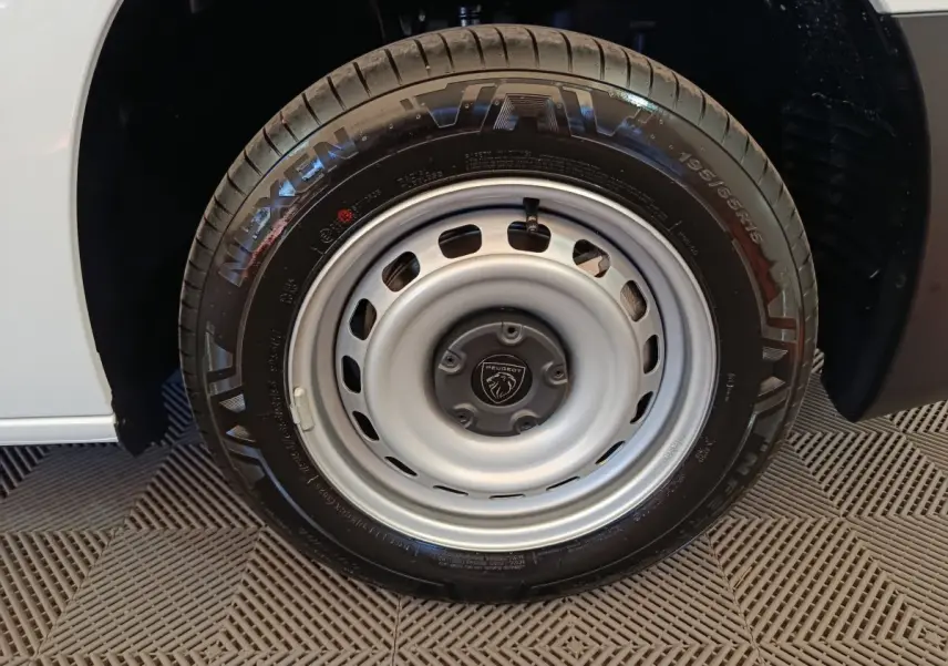 Gros plan sur la roue avant droite du Peugeot Partner blanc 2025 avec jante acier et logo Peugeot central.