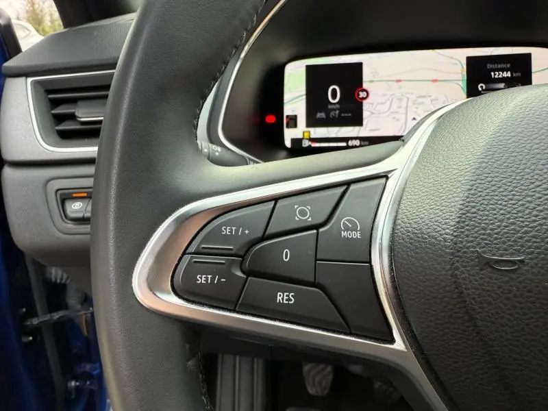 Gros plan sur le volant côté gauche du Renault Captur 2025 Bleu Iron/Noir Etoilé avec commandes de régulateur et tableau de bord numérique.