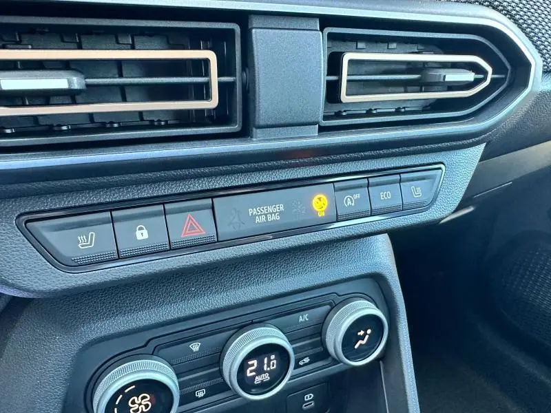 Vue rapprochée du tableau de bord de la Dacia Sandero beige Safari, montrant les commandes climatisation et alertes passager.