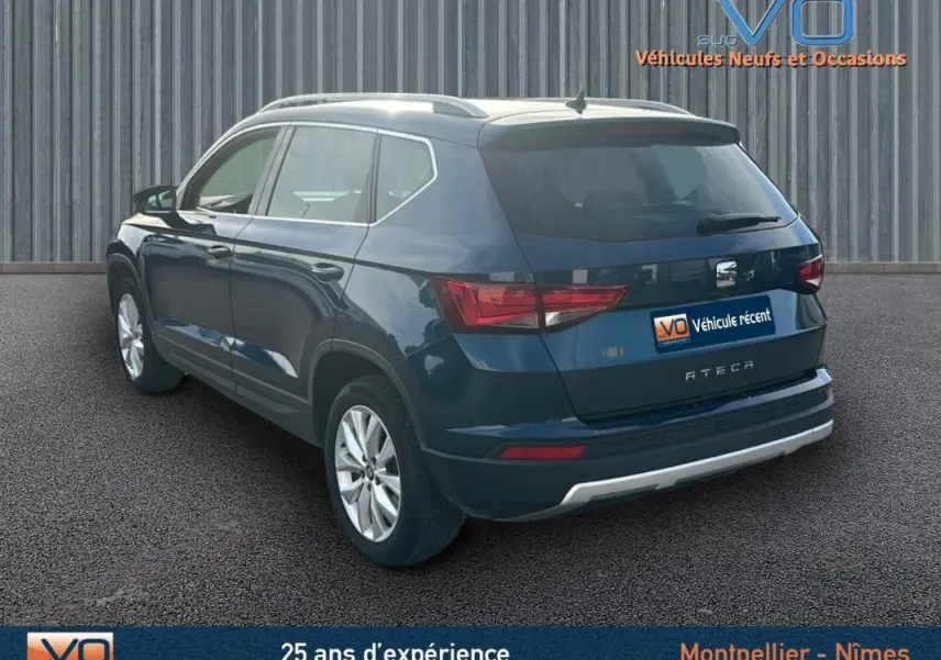 Vue 3/4 arrière droite d'un SEAT Ateca bleu foncé avec jantes alliage et barres de toit visibles.