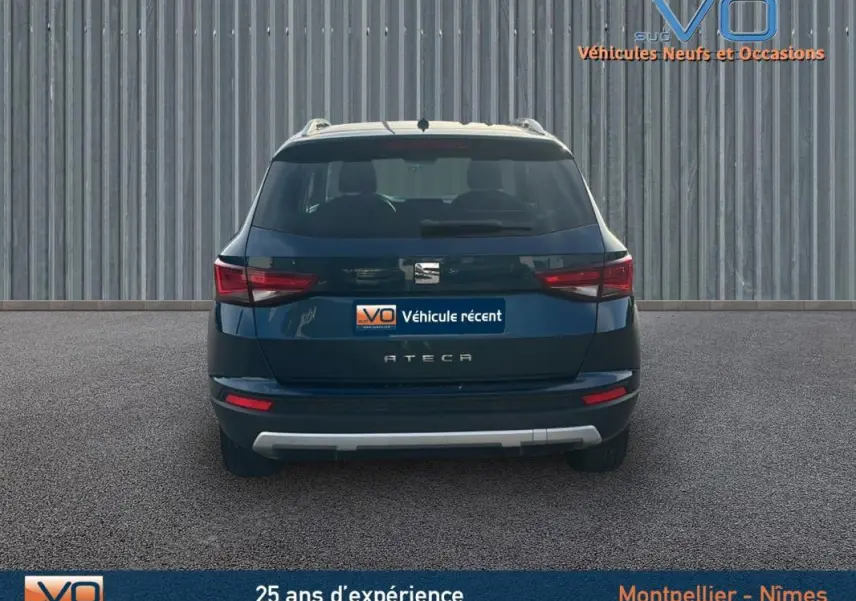 Vue arrière d'un SEAT Ateca bleu foncé avec feux arrière allumés et logo central visible sur fond industriel.