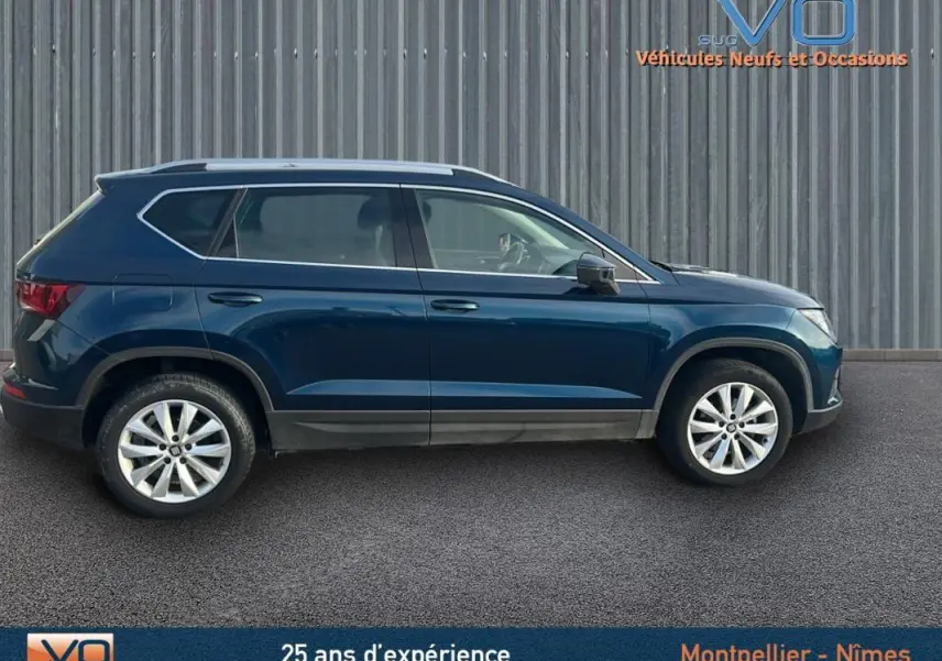 Profil latéral droit d'un SUV SEAT Ateca bleu foncé avec jantes alliage 17 pouces, stationné devant un mur métallique.