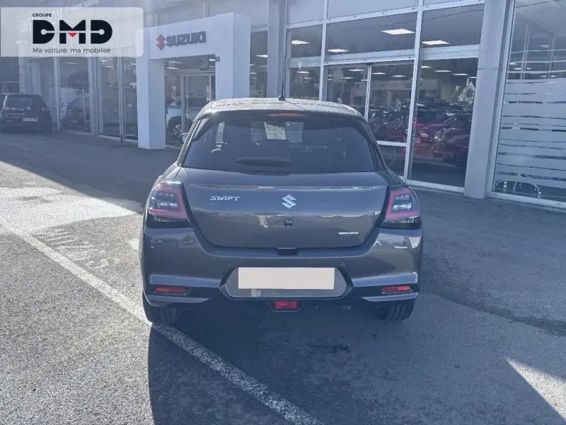 Vue arrière d'une Suzuki Swift 1.2 Hybrid 83ch Privilège 2024 en Mineral Gray Metal stationnée devant un showroom.