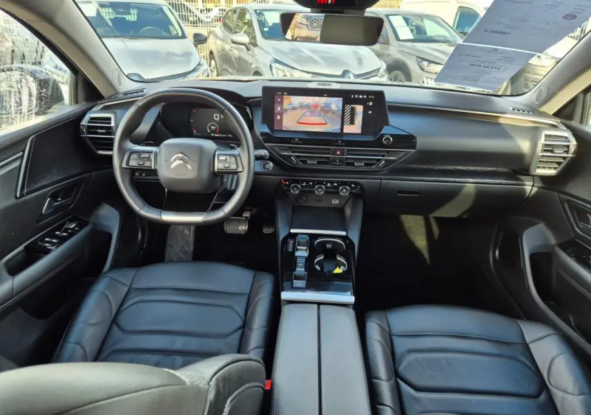 Vue intérieure avant de la Citroën C5 X 2024 noire, montrant le tableau de bord avec écran tactile et volant multifonction cuir.