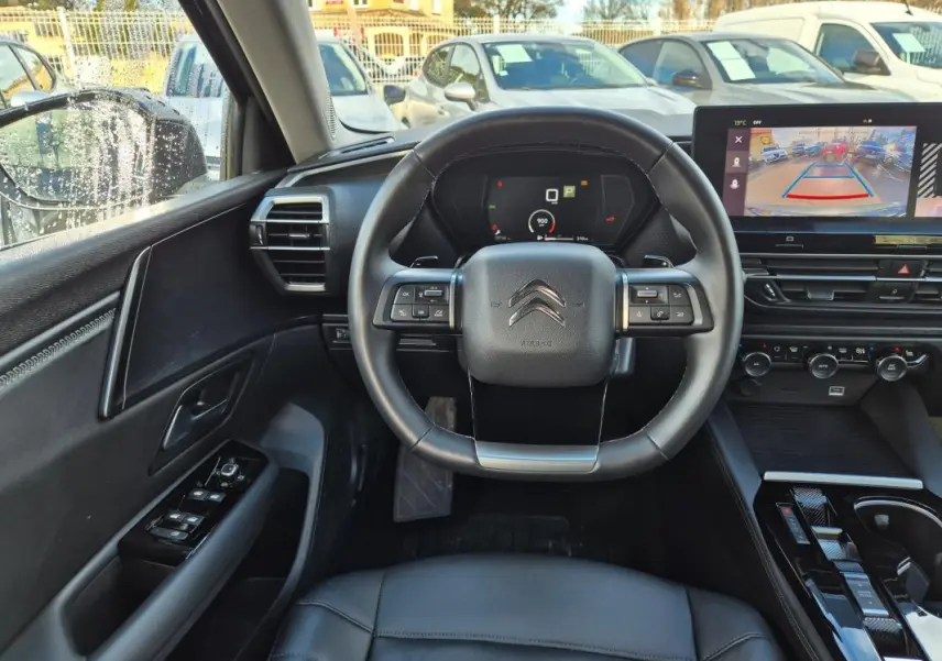 Vue intérieure centrée sur le volant cuir de la Citroën C5 X noire, avec tableau de bord digital et écran de caméra de recul.