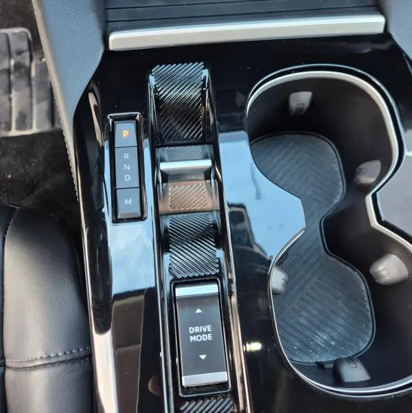 Vue rapprochée de la console centrale noire brillante de la Citroën C5 X 2024 avec sélecteur de boîte auto et commandes Drive Mode.