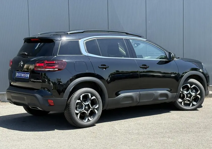 Vue 3/4 arrière droite d'un Citroën C5 Aircross Hybrid noir Perla avec jantes alliage bi-ton et barres de toit noires.