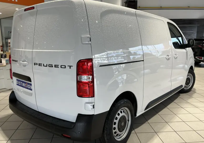 Vue 3/4 arrière droite d’un Peugeot Expert Fourgon blanc 2024 en showroom avec feux arrière rouges et pare-chocs noir.