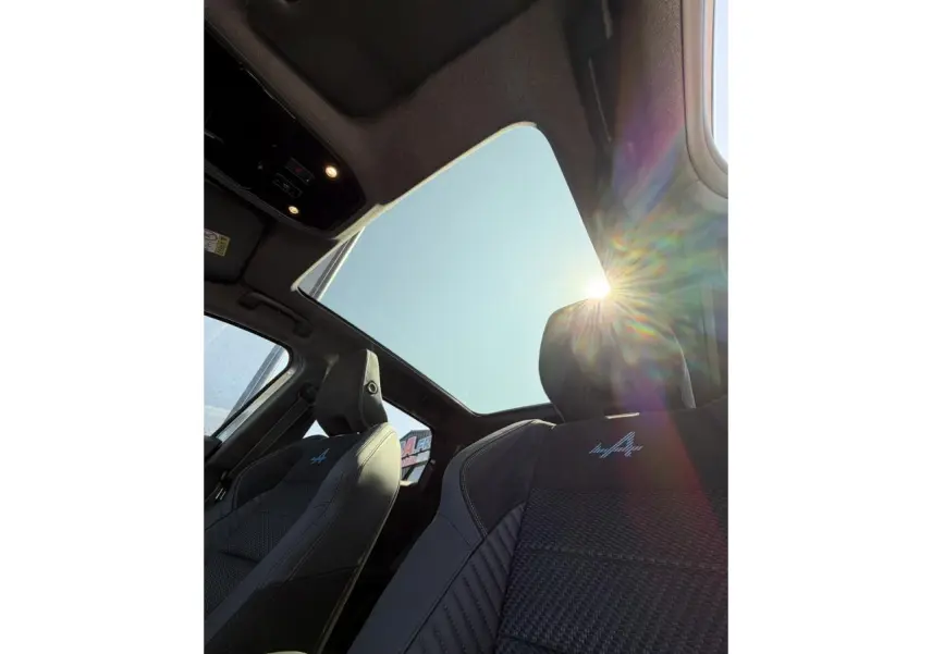 Vue intérieure en contre-plongée du toit panoramique et des sièges avant noirs avec logo Alpine brodé sur Renault Austral E-Tech.