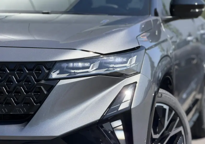 Gros plan sur l'avant droit gris schiste du Renault Austral 2026, mettant en valeur le phare LED et la calandre noire géométrique.