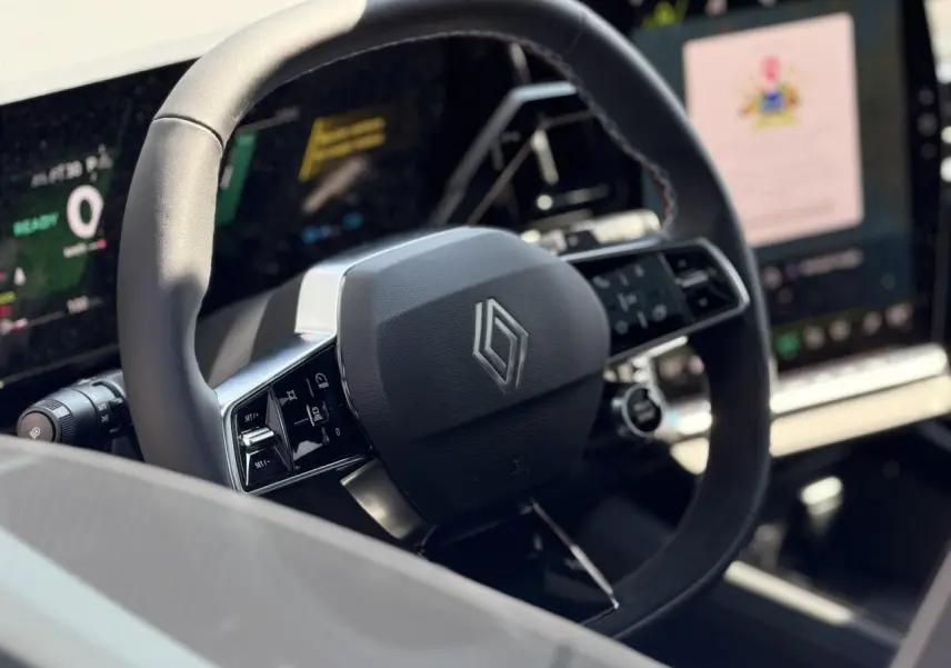 Vue rapprochée du volant noir au design moderne avec logo Renault, écran numérique et commandes intégrées visibles.