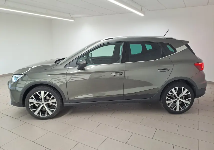 Vue de profil côté gauche d'un SEAT Arona gris falaise 2024 avec jantes alliage 18'' et vitres arrière surteintées.