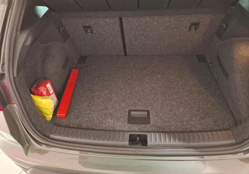 Coffre ouvert vu de l'arrière d'un SEAT Arona gris falaise 2024, avec tapis gris et kit de sécurité rangé à gauche.