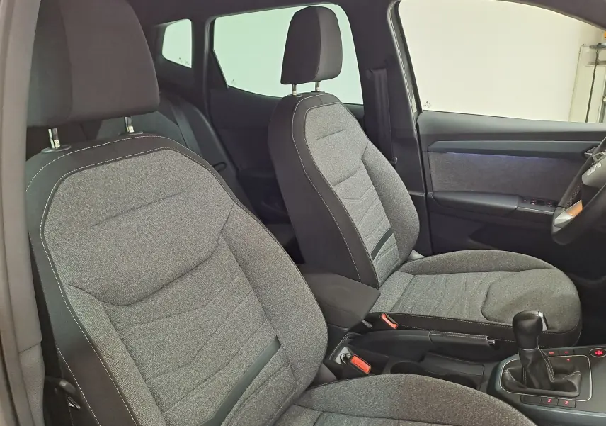 Vue intérieure côté avant droit du SEAT Arona 2024, sièges tissu gris avec surpiqûres contrastantes et console centrale.